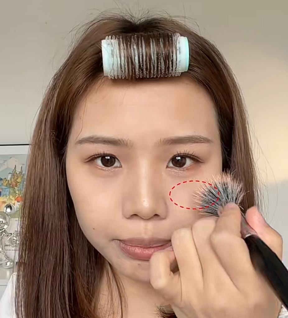 用大號修容掃沾取深色修容，於蘋果肌位置掃上胭脂。